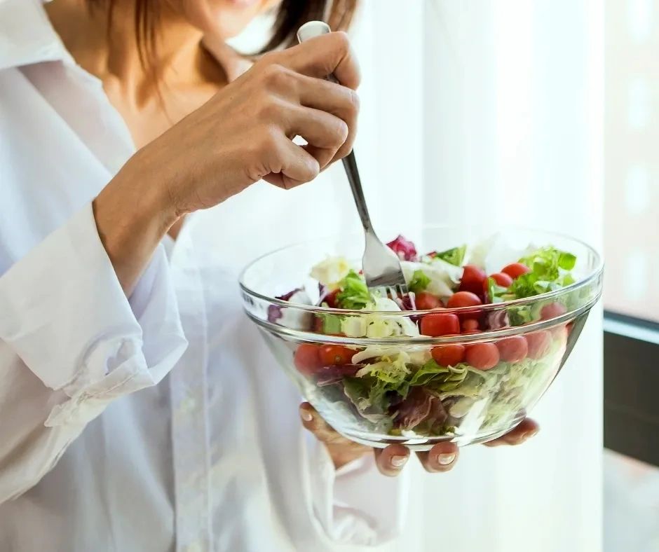 Person in white shirt eating fresh salad with cherry tomatoes and lettuce.