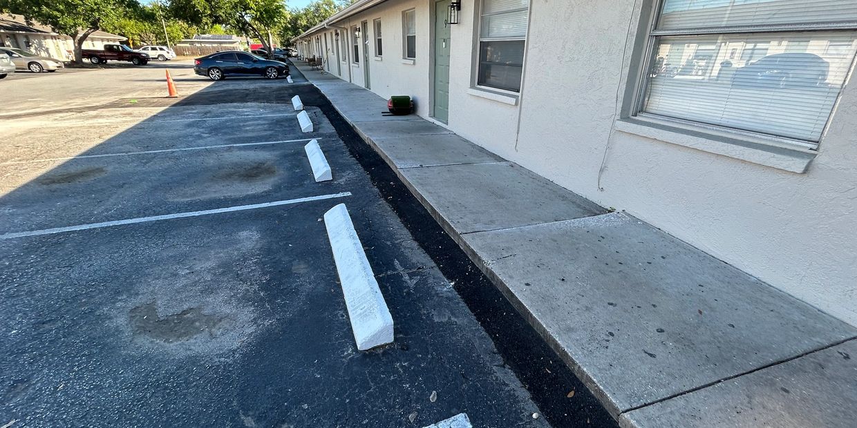 Empty parking spaces alongside a white apartment building on a sunny day.