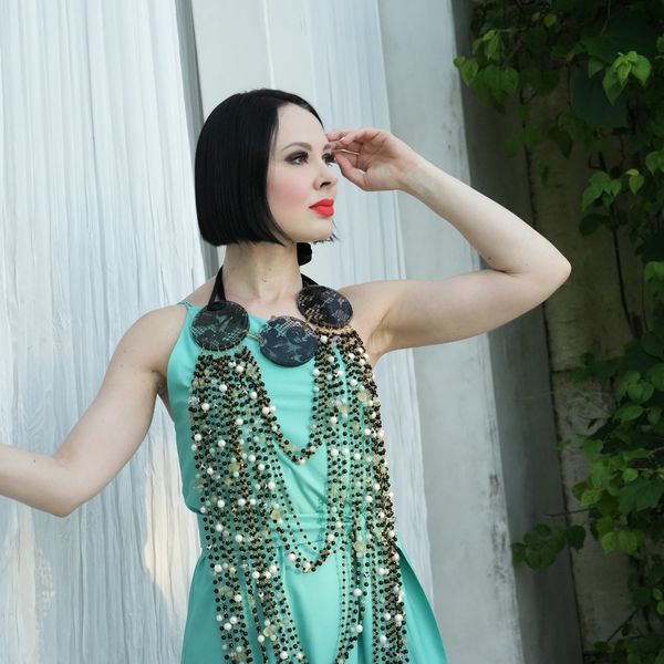 Woman in a turquoise dress with an elaborate beaded necklace posing gracefully.