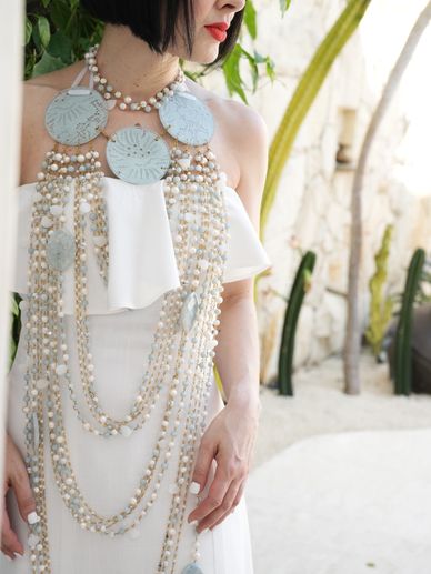 Woman in a white dress wearing an elaborate beaded necklace with large circular pendants.
