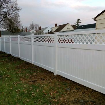 A long white vinyl fence with lattice top panels in a residential backyard.