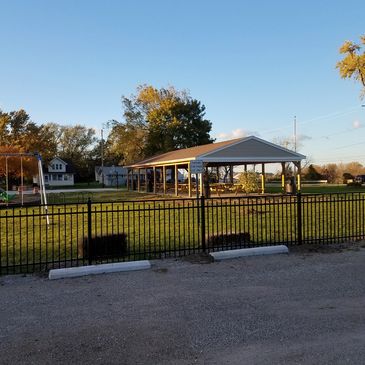 Open pavilion in a park with a black fence and clear sky.