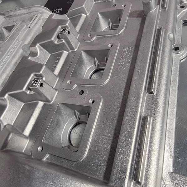 Close-up of a metallic machine part with intricate square recesses and mounting points.