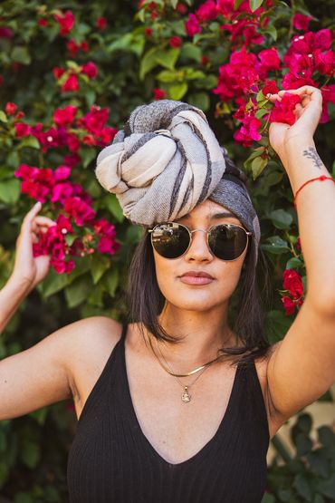 Woman with sunglasses and headwrap poses near vibrant red flowers.
