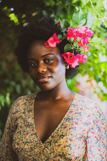 A woman with natural hair adorned with bright pink flowers and a floral dress.