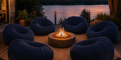 Cozy outdoor seating with bean bags around a fire pit at sunset by the water.