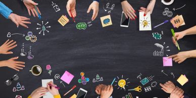 Hands collaborating around a blackboard filled with colorful business sketches and notes.