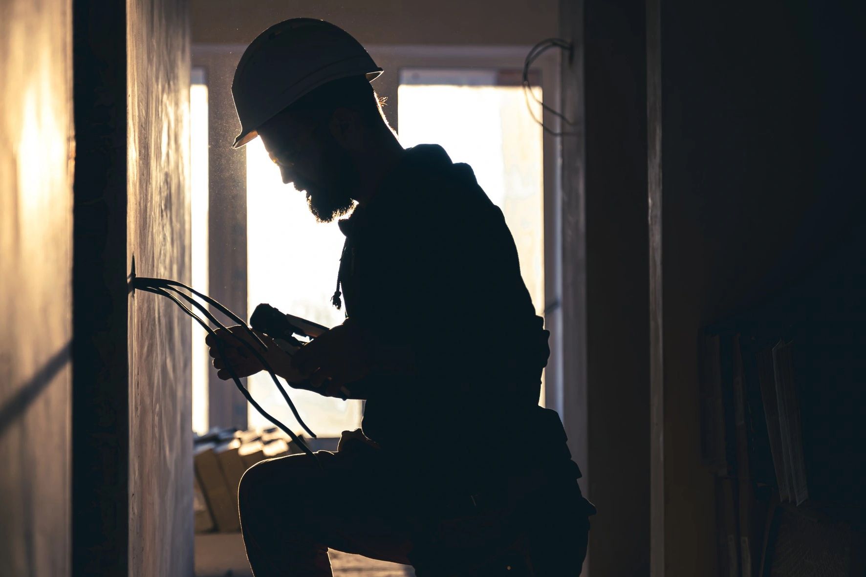 Silhouette of a construction worker inspecting wires in a dimly lit room.