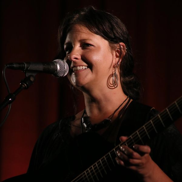 Woman singing and playing guitar on stage with a microphone.