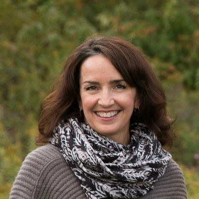 Kate Pecora smiling white woman  with long brown hair and brown eyes a grey shirt and cowl in front 