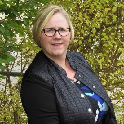 Tiffany King smiling white woman with short blond hair and glasses  and a black jacket with a black 