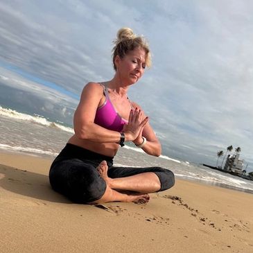 Woman practicing yoga on the beach with hands in prayer pose.
