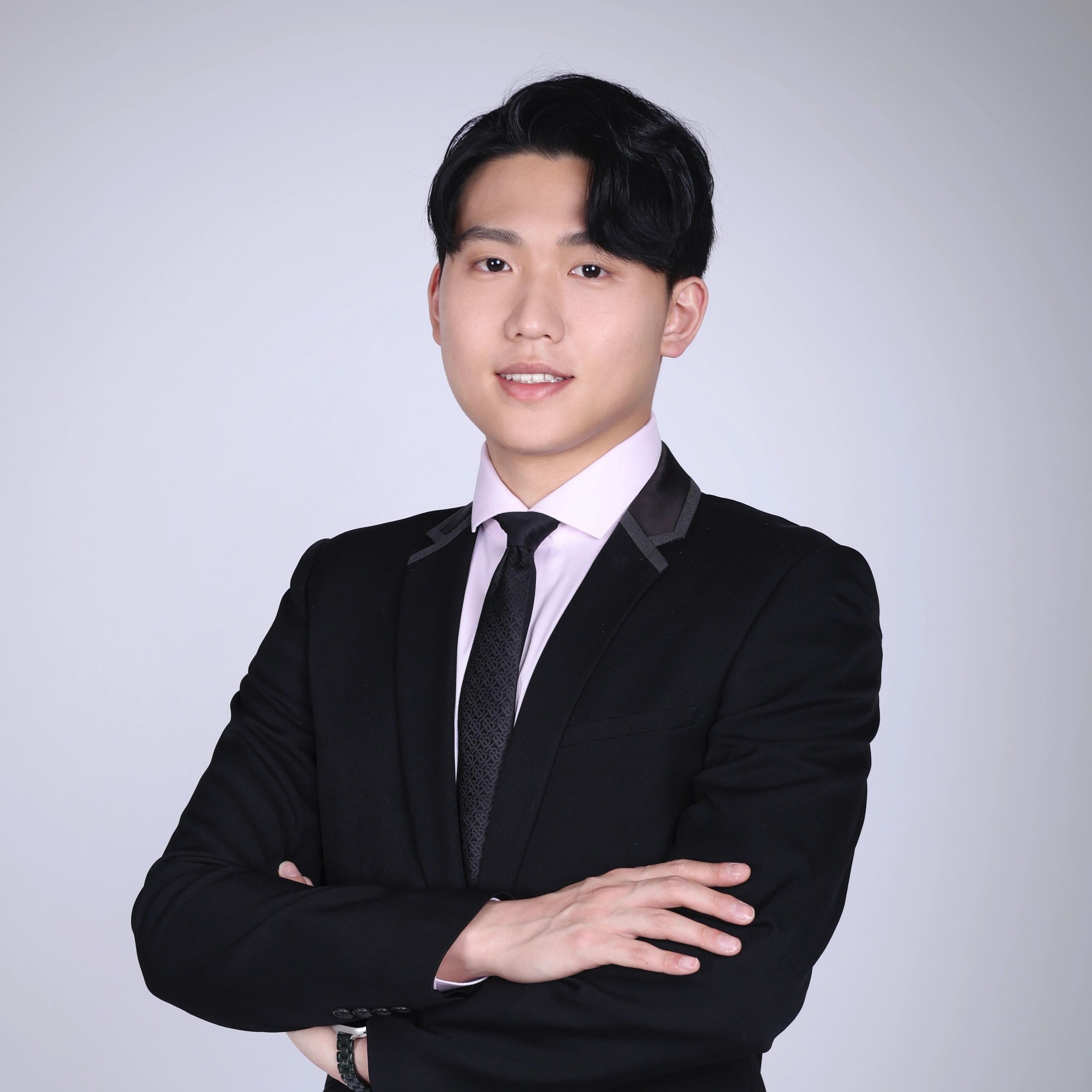 Confident young man in a black suit with arms crossed, smiling.