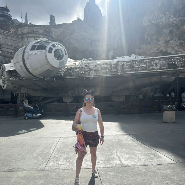 A woman posing in front of the Millennium Falcon on a sunny day.