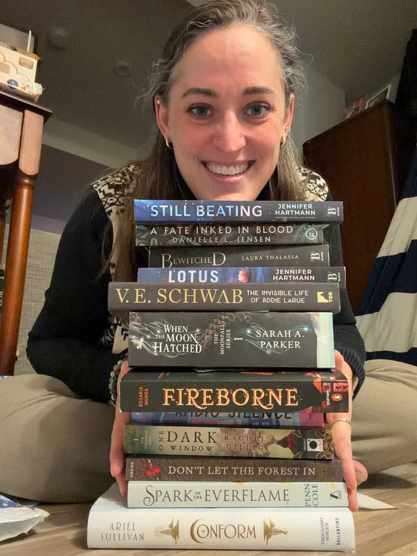 Person smiling behind a stack of books.