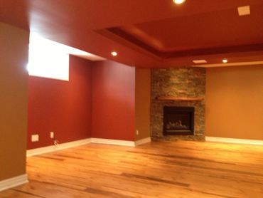 Empty basement room with a fireplace and hardwood floor.