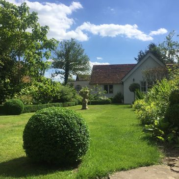 A sunny garden with neatly trimmed bushes and a small house.