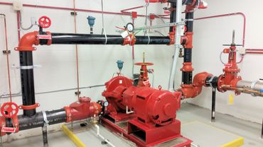Industrial red pump system with black pipes in a utility room.