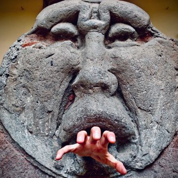 Hand reaching out from a stone face sculpture.