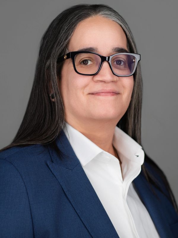 Person with glasses and long hair wearing a blue suit jacket.
