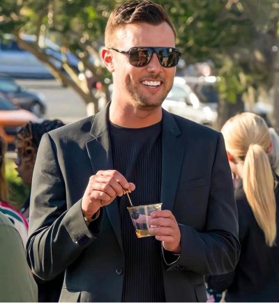 A stylish man in sunglasses enjoys a drink outdoors.