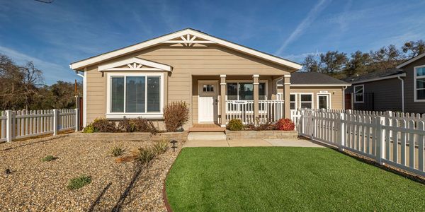 Single-story beige house with a white fence and mixed gravel and grass yard.