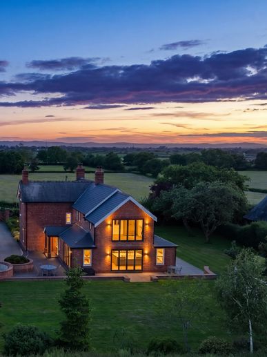 A warmly lit brick house at sunset in a peaceful rural setting.