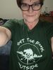 female with glasses wearing a dark green shirt with wording reading ' Get the f*ck outside'. 