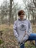 Female in the woods wearing a grey hoodie that reads Get the F*ck Outside.