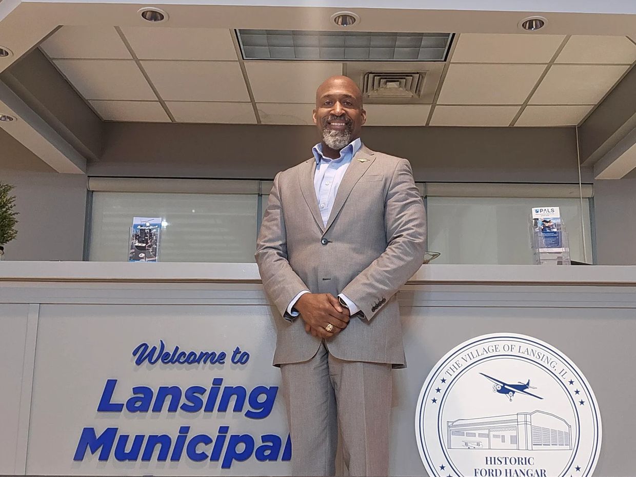 Man in a gray suit stands confidently at Lansing Municipal desk.