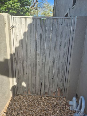 Weathered wooden gate between two walls with gravel ground.