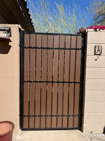 Brown wooden gate with black metal frame between beige walls under clear blue sky.