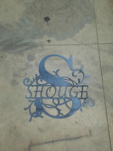 Decorative metal monogram with the name 'Shough' on concrete ground.