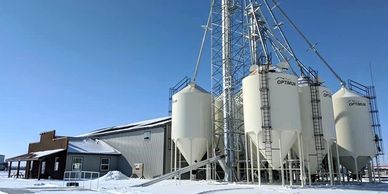 Snow-covered grain silos and a farm building under a clear blue sky.