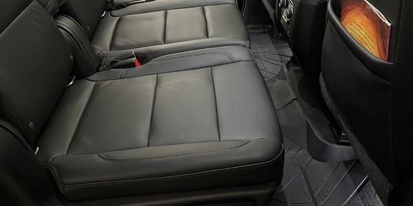 Clean black leather car seats with floor mats in the rear cabin.