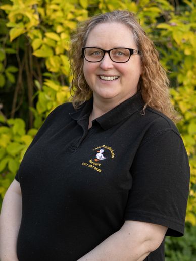 Smiling woman with glasses in a black polo shirt outdoors.