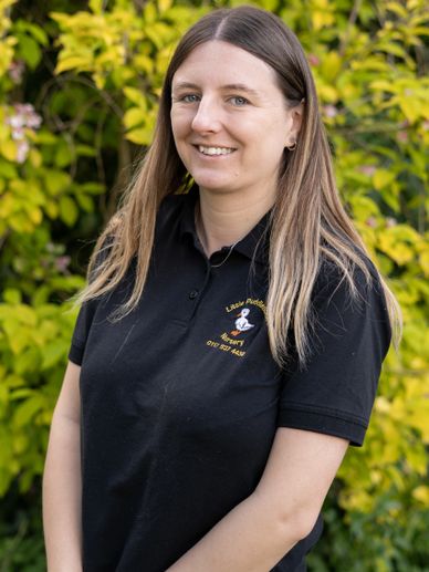 Smiling woman wearing a black polo shirt with nursery logo stands outdoors.