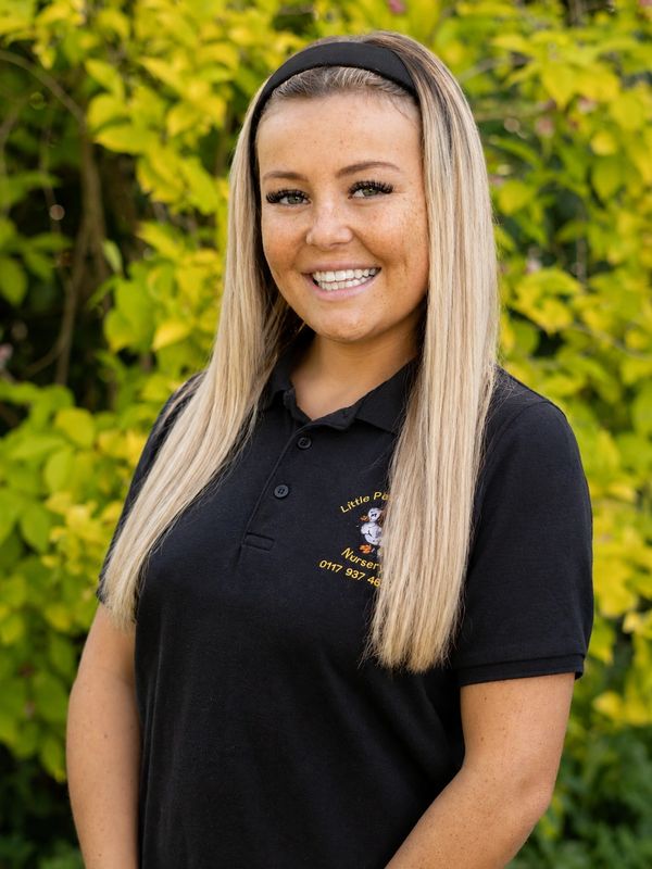 Smiling woman with long blonde hair wearing a black polo shirt outdoors.