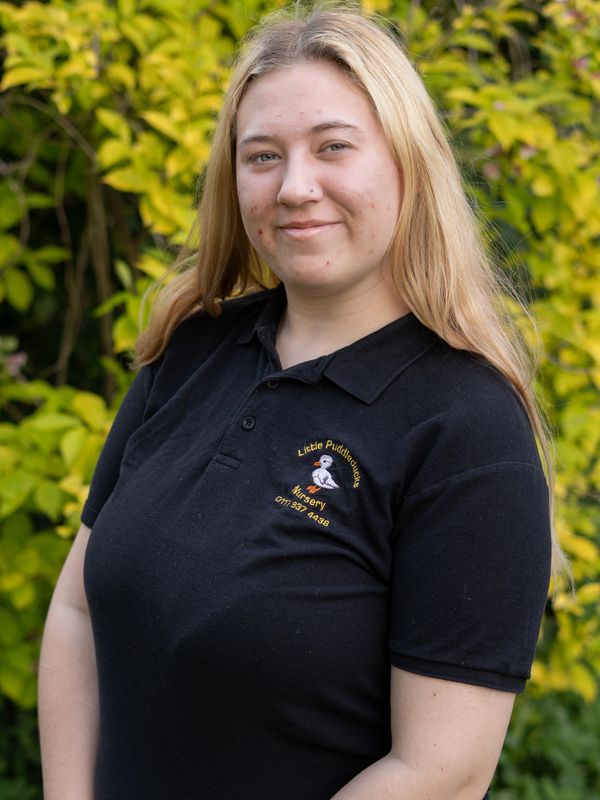 Young woman smiling in a black nursery polo shirt outdoors.
