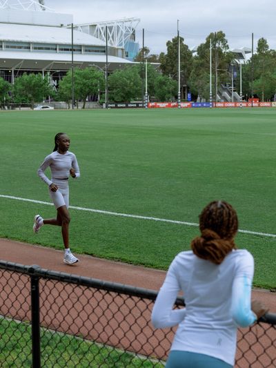 A young athlete jogging on a track with a coach watching nearby.