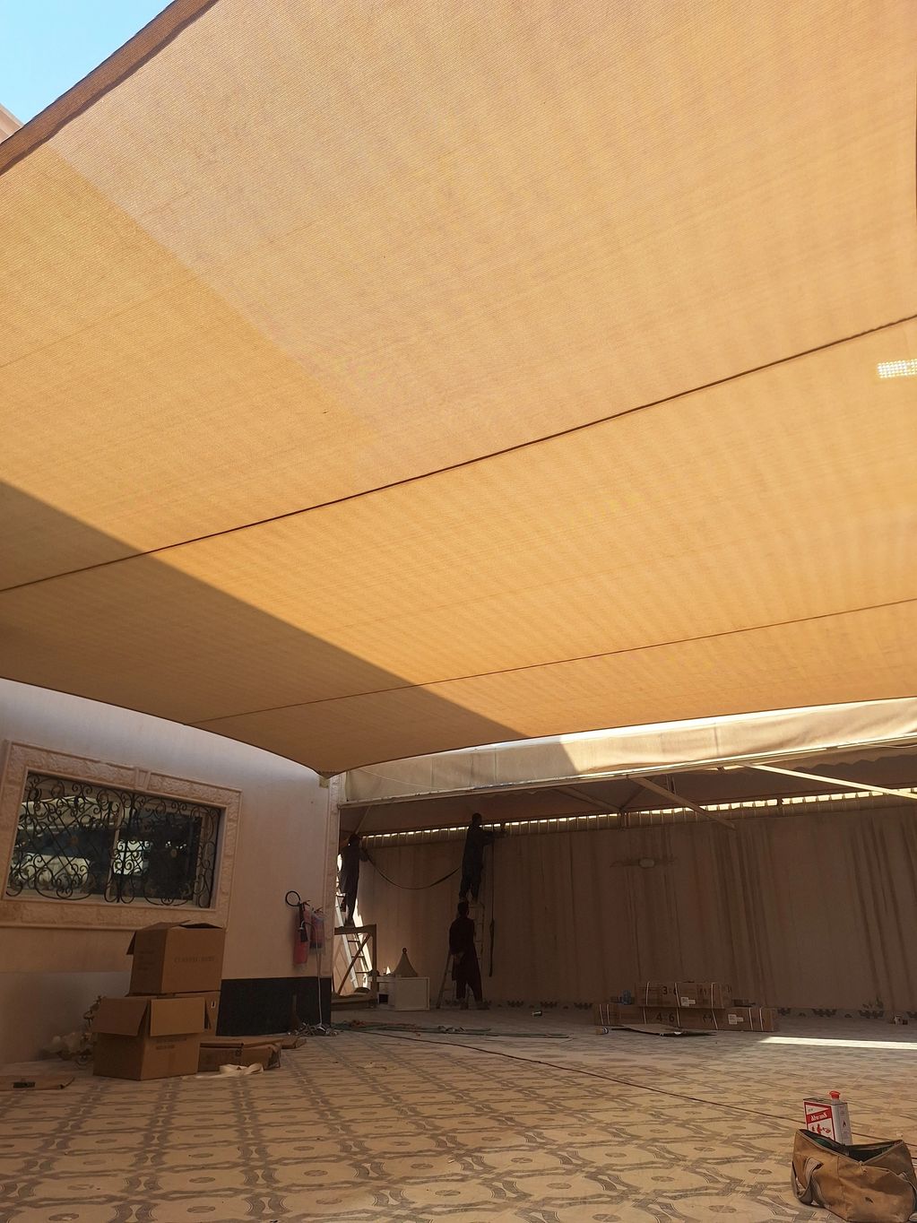 Workers installing a large beige sunshade canopy.