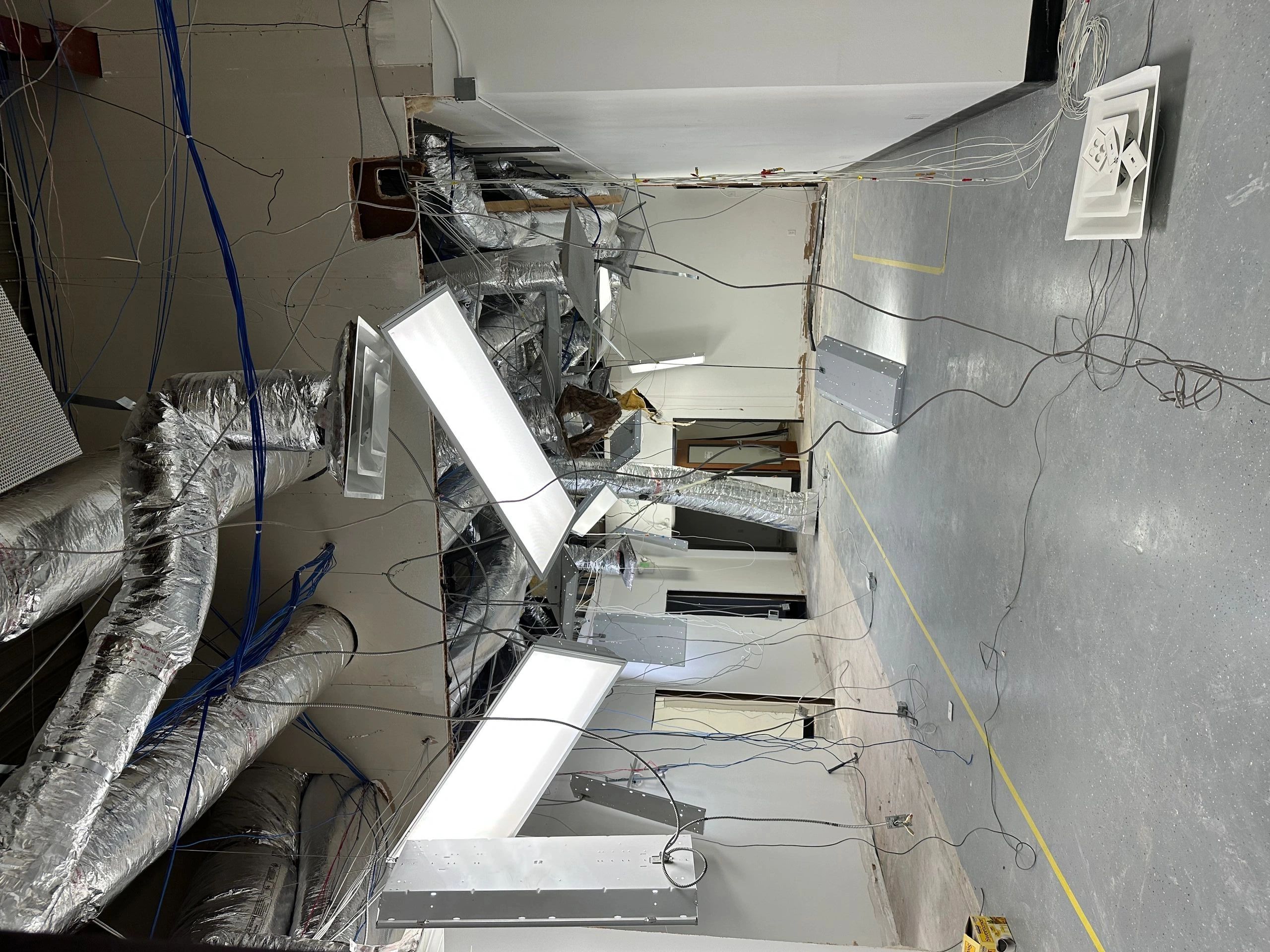 Exposed ceiling with hanging lights and ducts in a construction site.