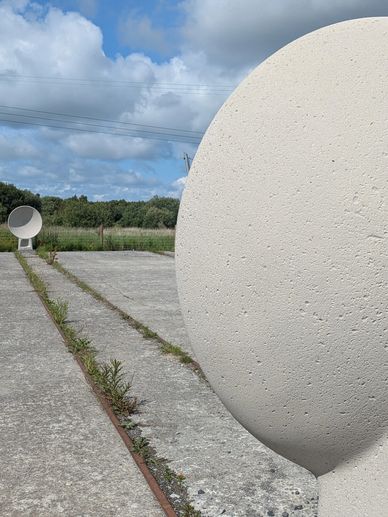 Two large, white, circular concrete sculptures on a paved pathway in an outdoor field.