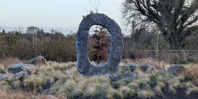 A large stone ring sculpture surrounded by grass and stones in a natural setting.