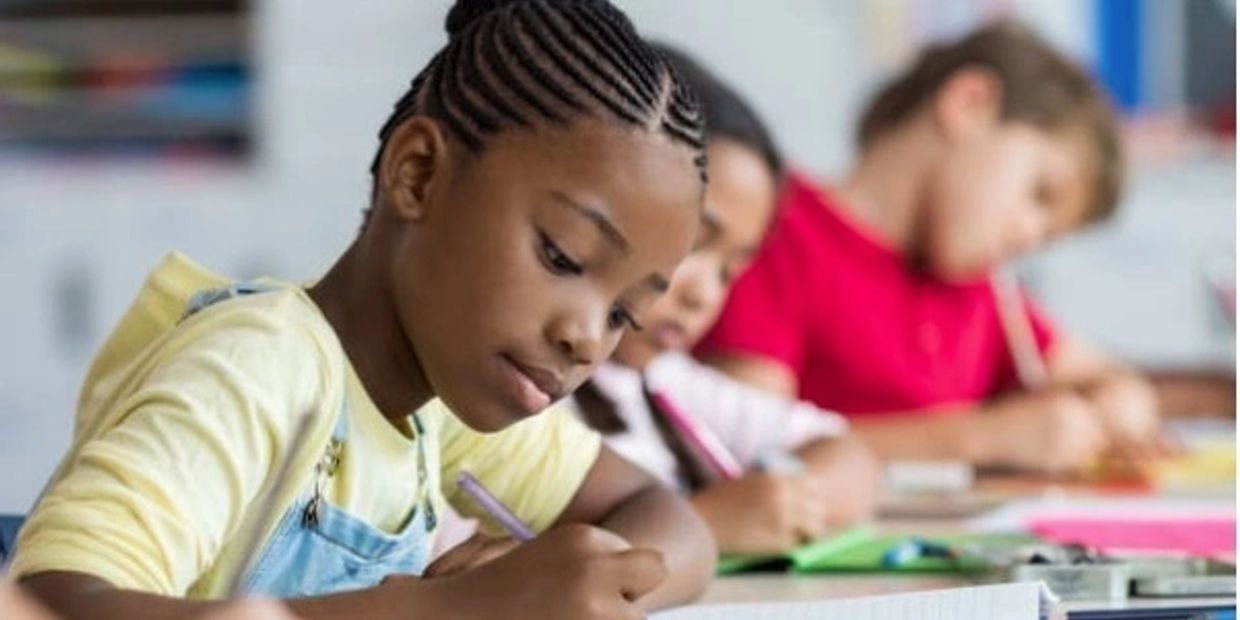 Children focused on writing at a classroom desk.