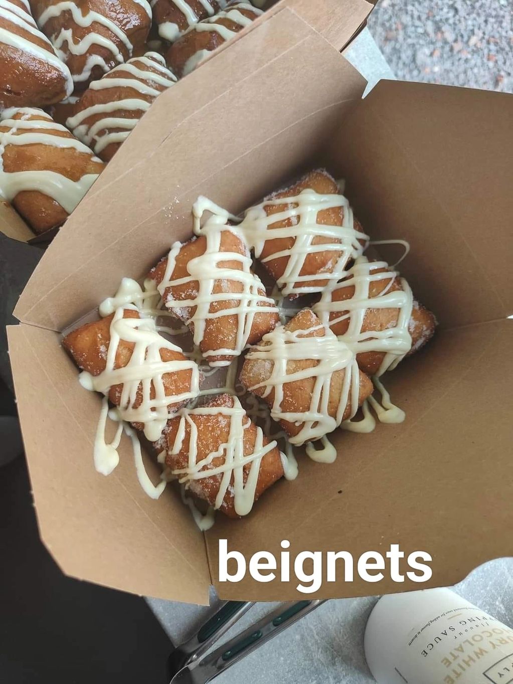 Beignets drizzled with white icing in a cardboard box.