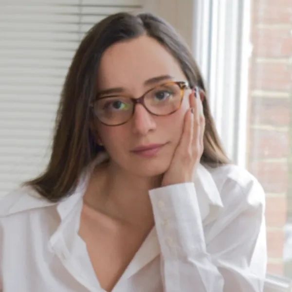Thoughtful woman with glasses resting her face on her hand indoors.