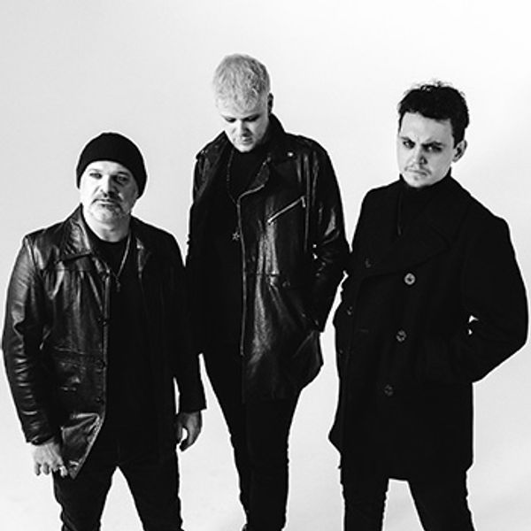 Three men dressed in black leather and coats in a studio.