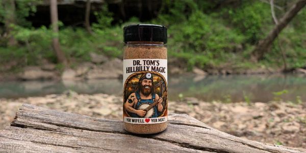 A spice bottle labeled "Dr. Tom's Hillbilly Magic" on a wooden surface outdoors.