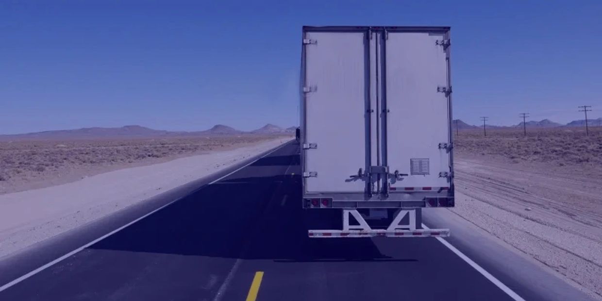 A truck driving on a deserted highway through a dry, barren landscape.